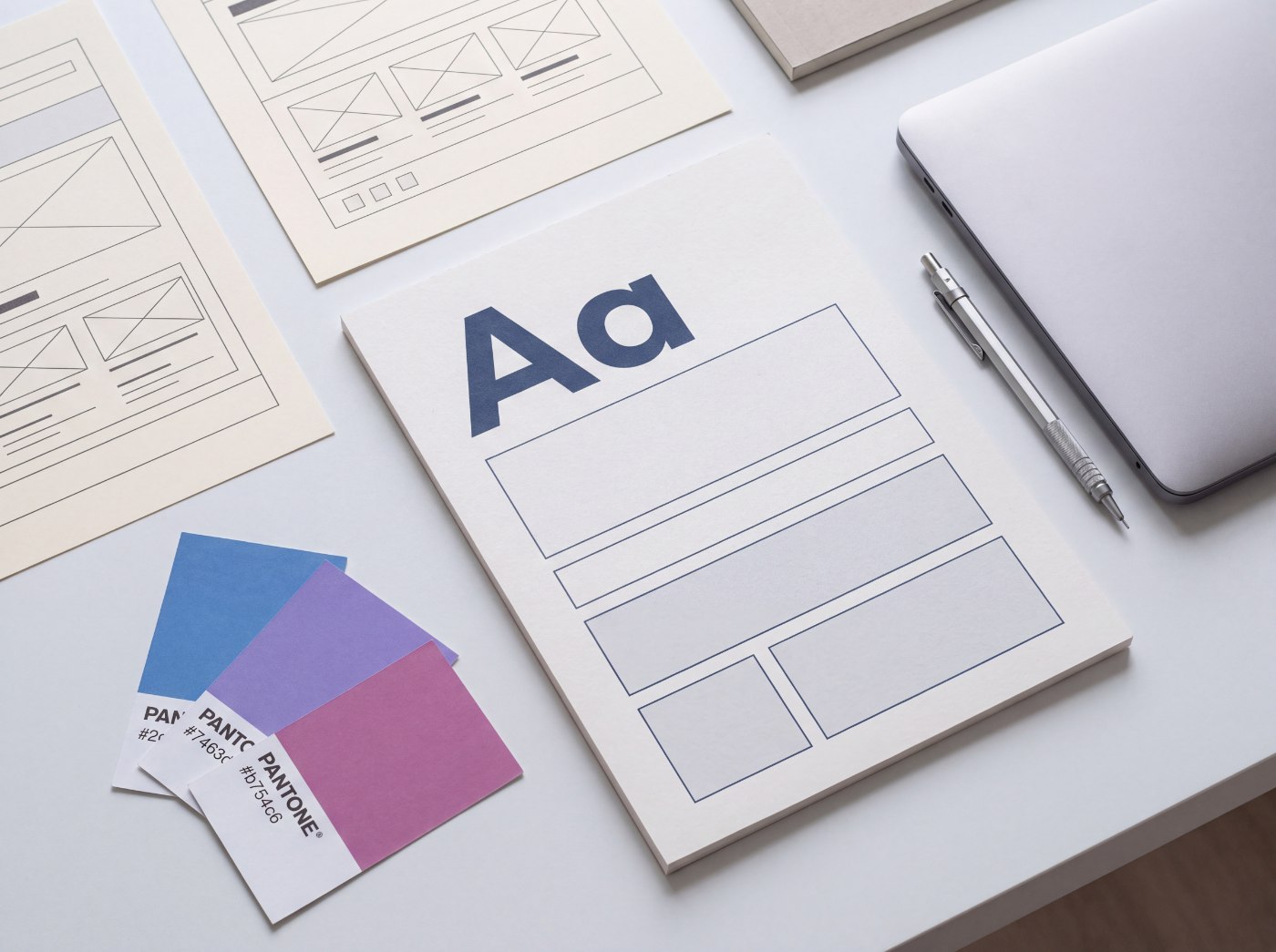 Arbeitsplatz mit Wireframe-Ausdrucken, Typografie-Muster Aa und Farbmusterkarten